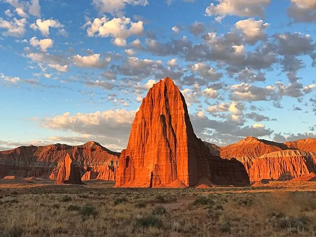 A towering red sandstone monolith rising from a desert valley.