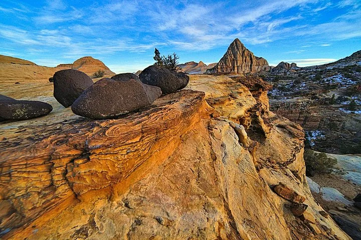 Dunkle vulkanische Felsbrocken auf einem geschichteten, sonnenbeschienenen Sandsteingrat.