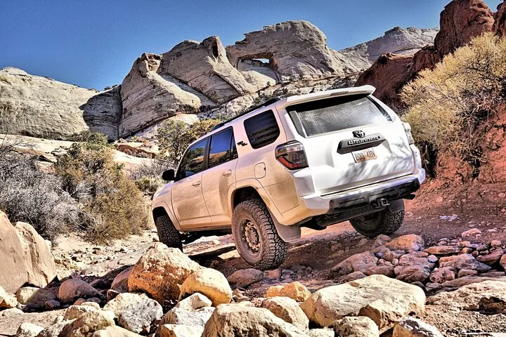 Ein weißer Toyota SUV erklimmt einen felsigen Pfad in der Nähe eines Felsbogens.