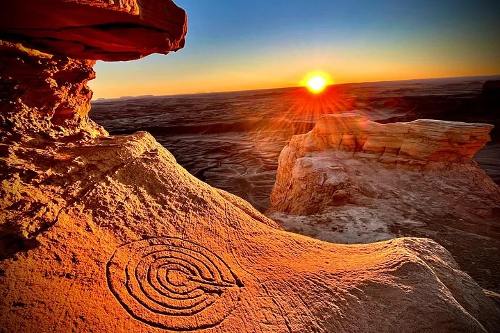 A spiral petroglyph carving on a rock at sunset.