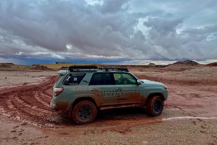 A muddy off-road vehicle parked in a desert landscape under cloudy skies.