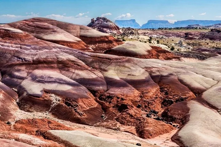 Rolling, multi-colored banded dunes of Bentonite Hills with distant cliffs.