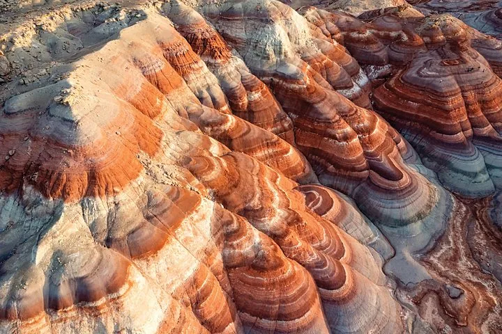 Vista aérea de Bentonite Hills que muestra distintas capas de roca rojas, blancas y grises